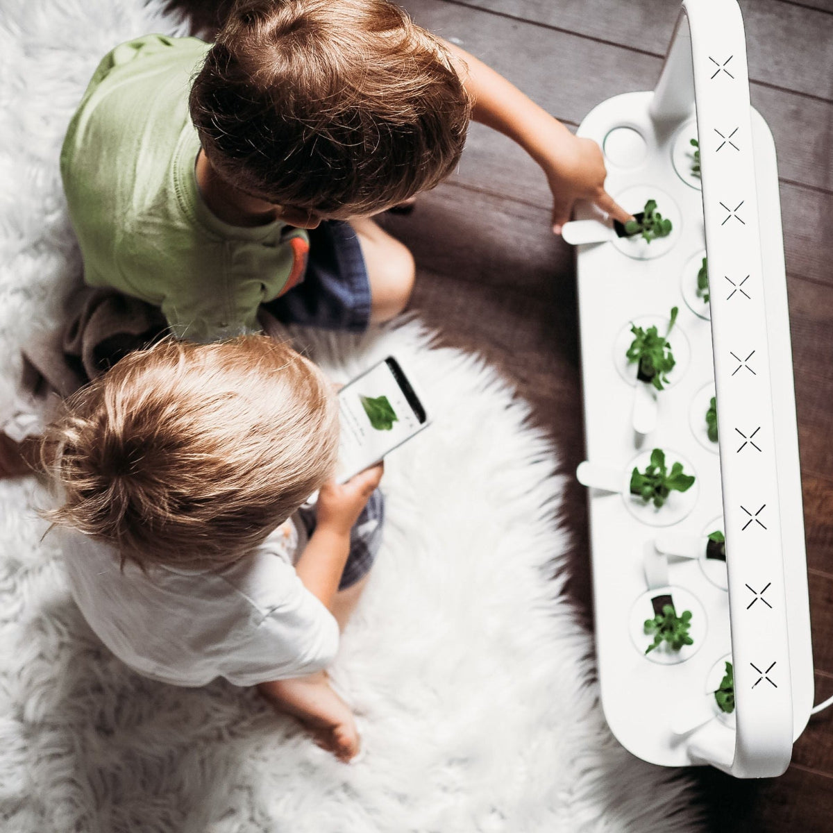 The Smart Garden 9 / Two children interacting with a small indoor gardening setup on a wooden floor.