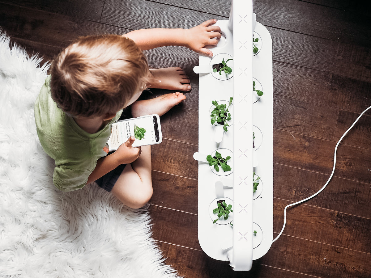 The Smart Garden 9 / A young boy sitting on the floor next to a Click and Grow Smart Garden 9.